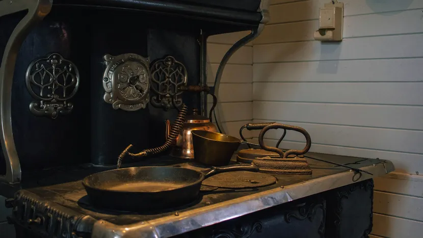 An antique cast iron range with a skillet and a copper kettle.