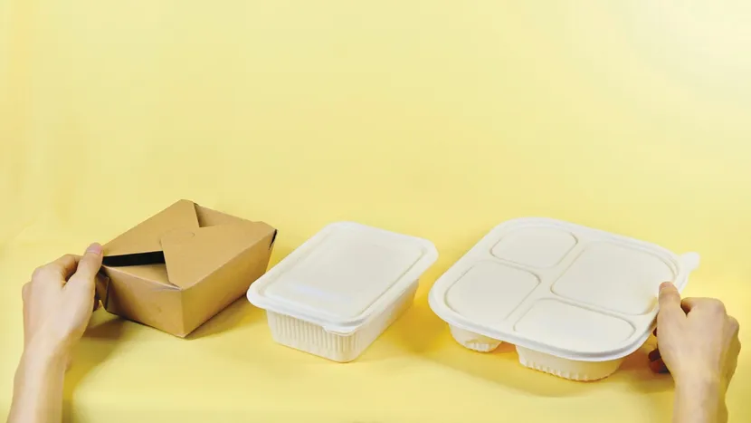 Hands holding an open takeout box and two sealed containers.