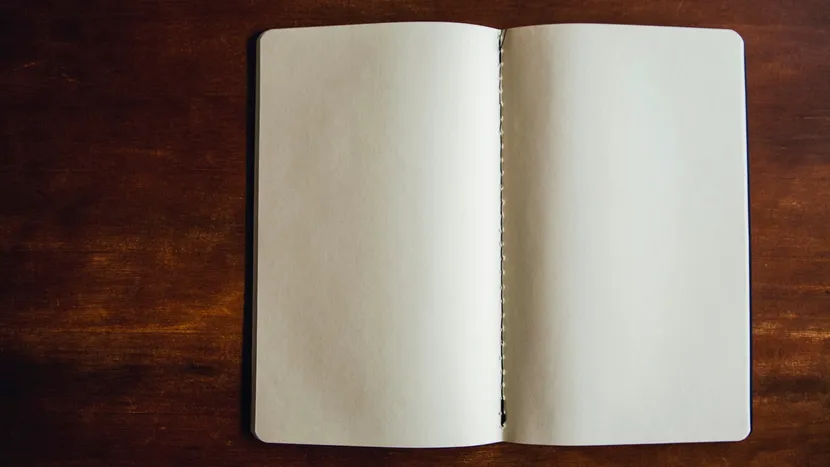 An open notebook with blank pages resting on a dark wooden table.