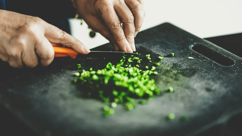 Hands chopping spring onions on a board with a small knife.