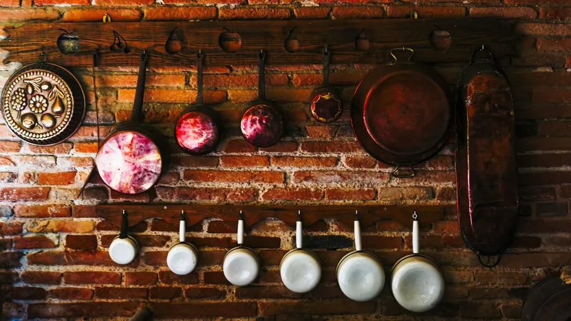 Copper pans and a row of white enamel saucepans hanging in order on a brick kitchen wall.