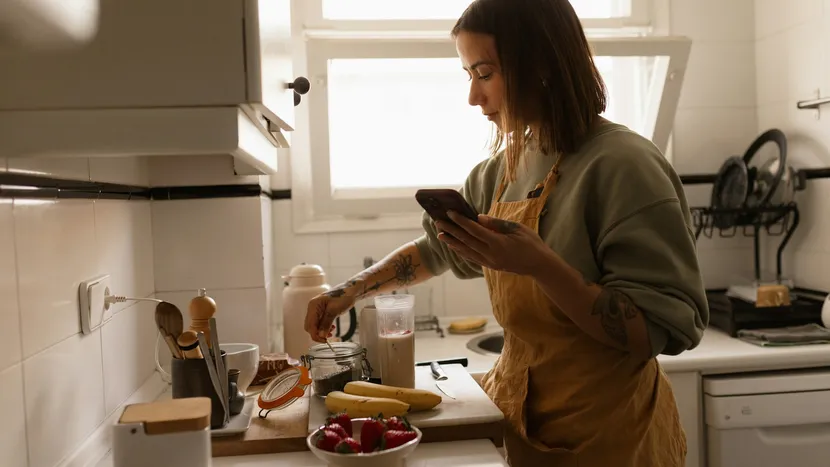 Someone in a kitchen following a recipe on their phone while preparing a smoothie.