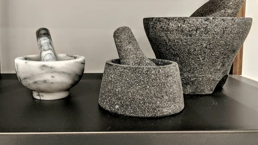 Three stone and marble mortars with their pestles on a dark counter.