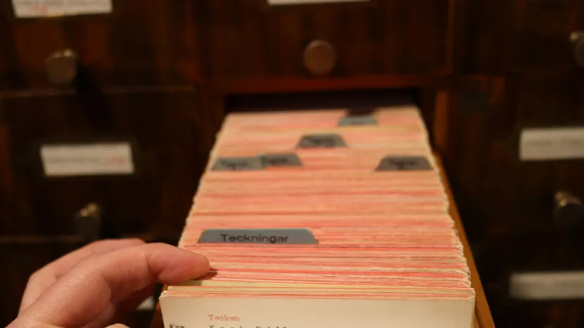A hand pulling a card from a large wooden index card drawer.