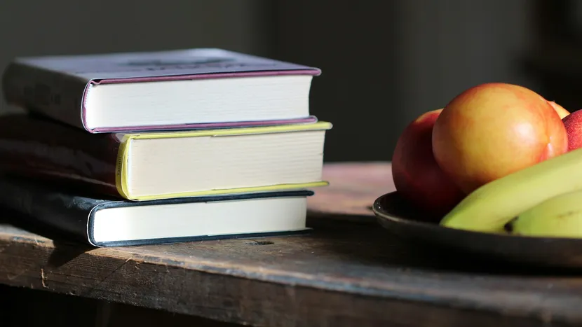 A stack of three books beside a plate of fruit on a wooden table.