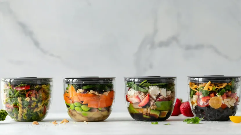 Four sealed containers of prepared salads lined up on a counter.